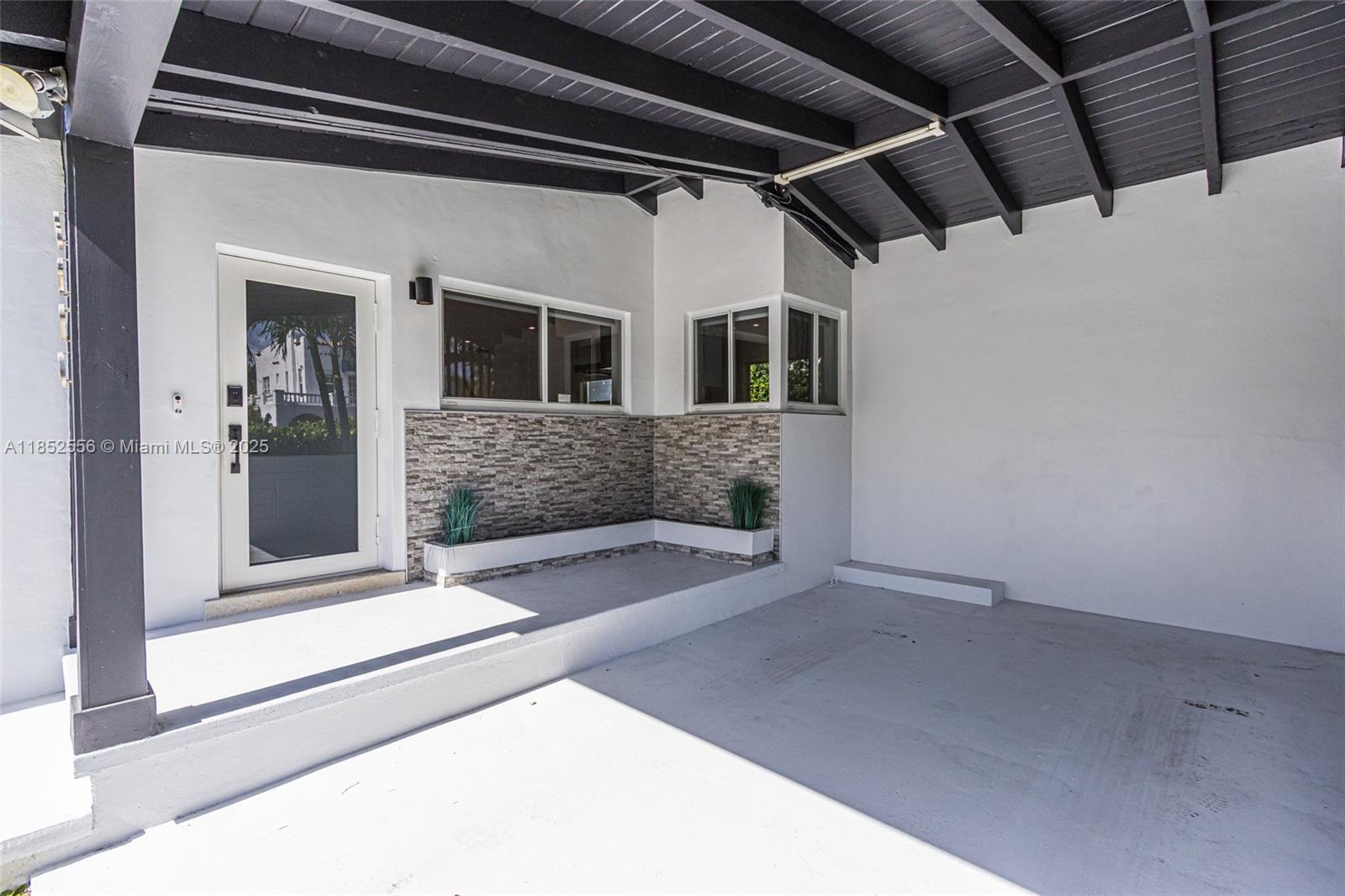 A covered patio features a white concrete floor, stone-accented walls, and a dark wood ceiling — 8290 N Bayshore Dr, Miami FL 33138, MIAMI, FL