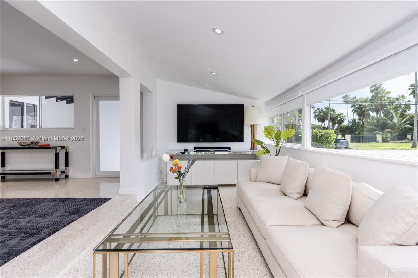 A living room features a white sofa, glass coffee table, and a wall-mounted television — 8290 N Bayshore Dr, Miami FL 33138, MIAMI, FL