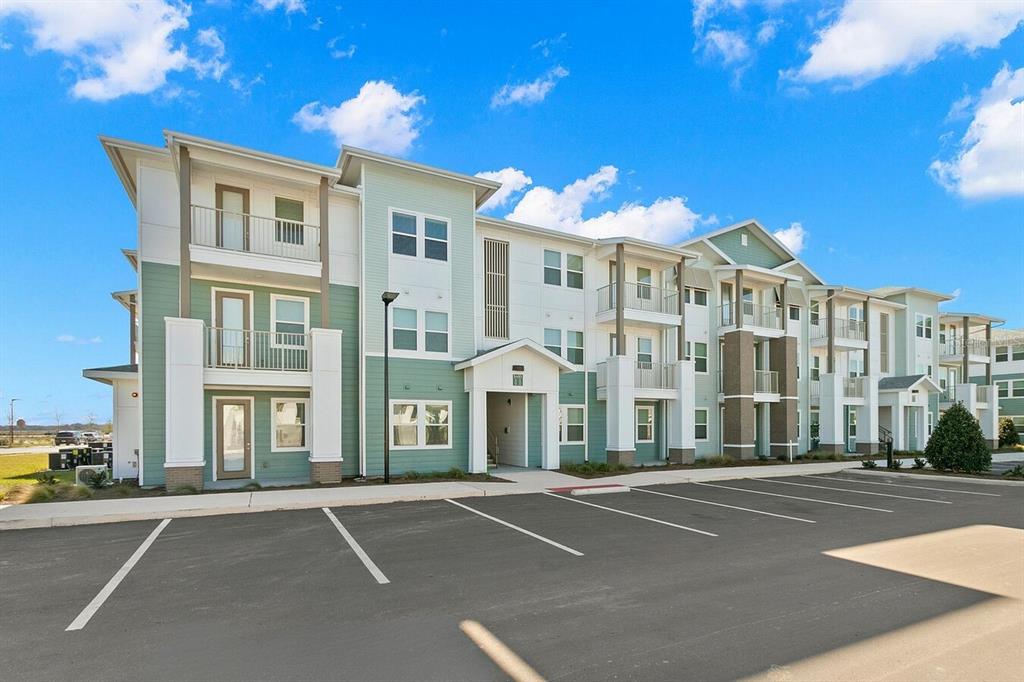 A three-story apartment building with light green and white siding stands beside a paved parking lot — 5476 ANGEL WAY UNIT B1, ST CLOUD, FL