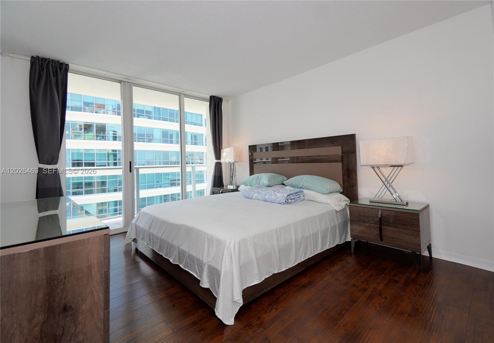 A bedroom features a platform bed, dark wood flooring, and floor-to-ceiling windows overlooking buildings — 1155 Brickell Bay Dr # 3301, Miami FL 33131, MIAMI, FL