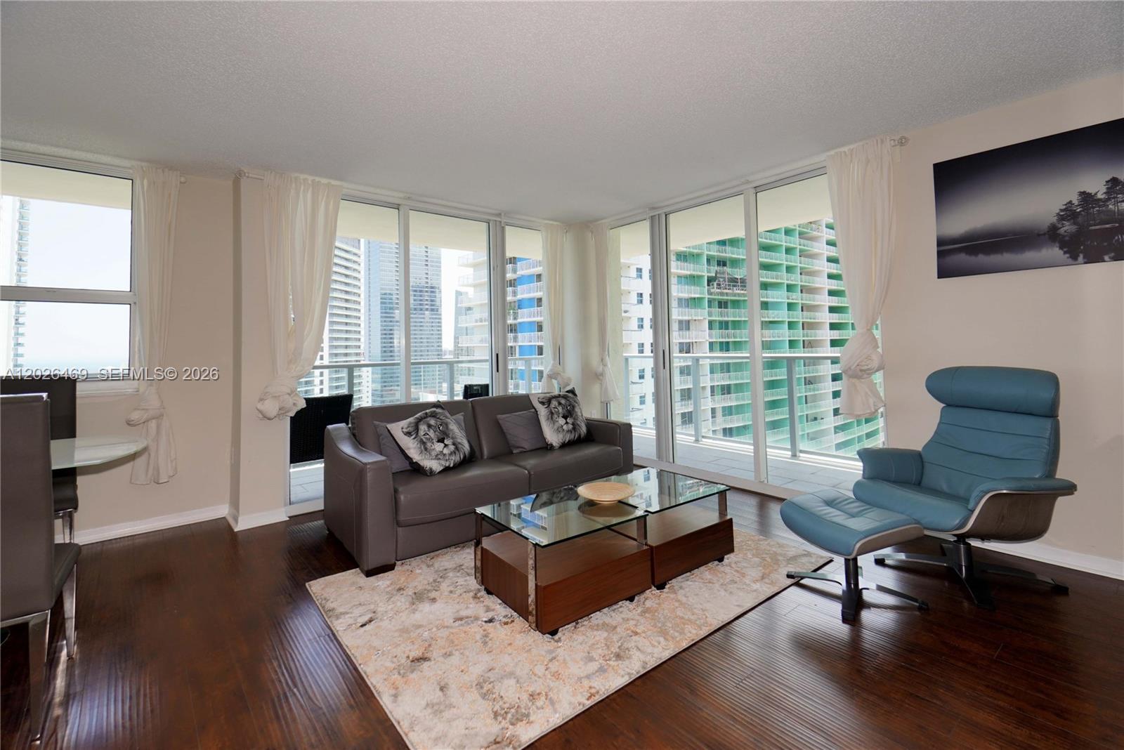 A living room features dark wood floors, a grey sofa, and a blue lounge chair — 1155 Brickell Bay Dr # 3301, Miami FL 33131, MIAMI, FL