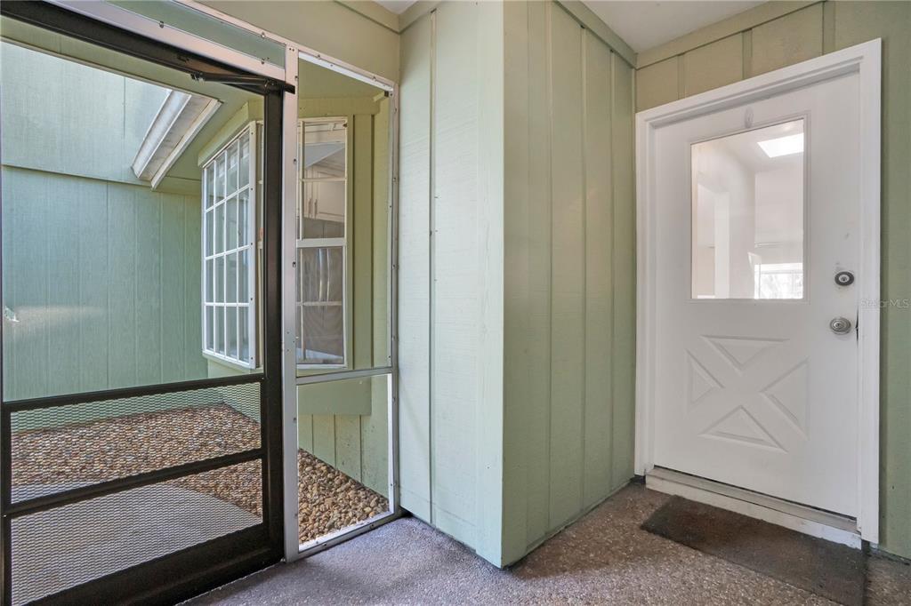 A white entry door sits next to a screened-in porch area with gravel flooring — 16 EAGLE LANE, NEW SMYRNA BEACH, FL