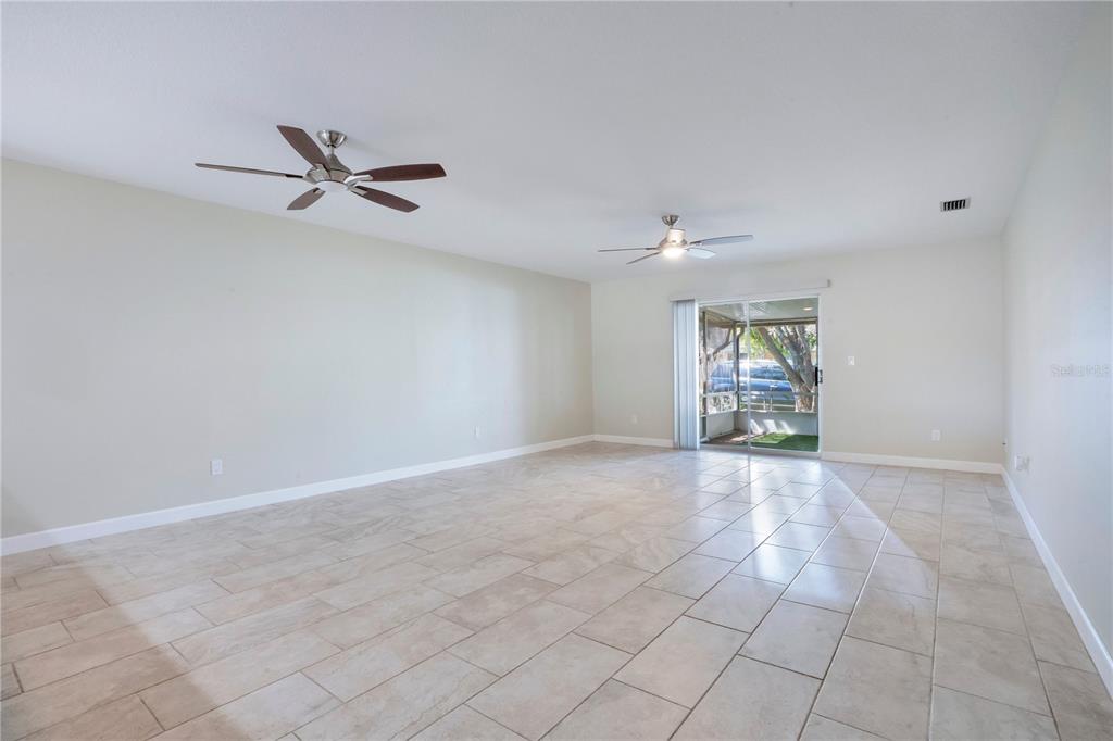 An empty living room features light-colored tile flooring, two ceiling fans, and a sliding glass door — 16 EAGLE LANE, NEW SMYRNA BEACH, FL
