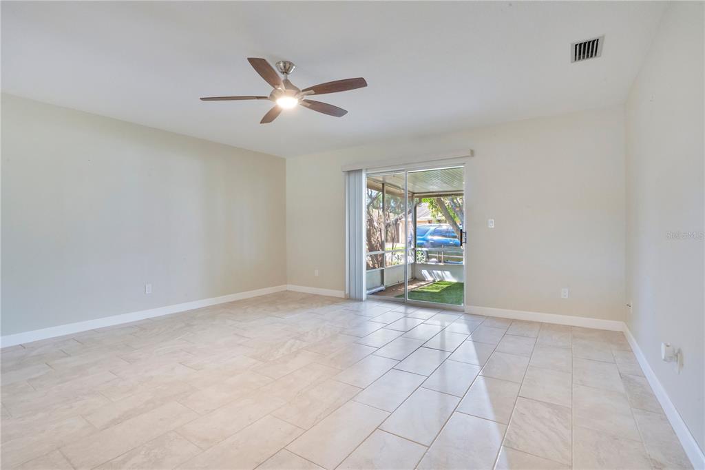An empty living room with light tile flooring, a ceiling fan, and sliding glass doors — 16 EAGLE LANE, NEW SMYRNA BEACH, FL
