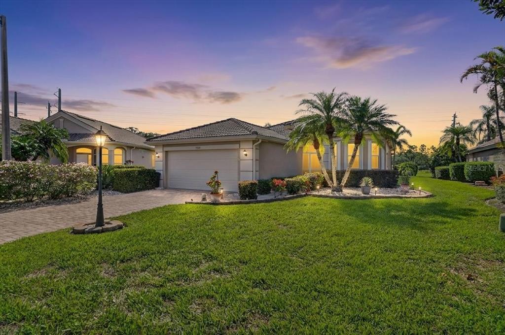 A single-story house with a two-car garage, palm trees, and a paved driveway at sunset — 7128 DREWRYS BLUFF, BRADENTON, FL