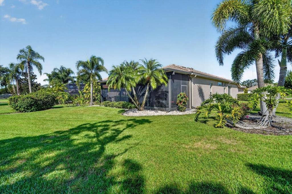 A grassy backyard features a house with a screened-in lanai and several palm trees — 7128 DREWRYS BLUFF, BRADENTON, FL