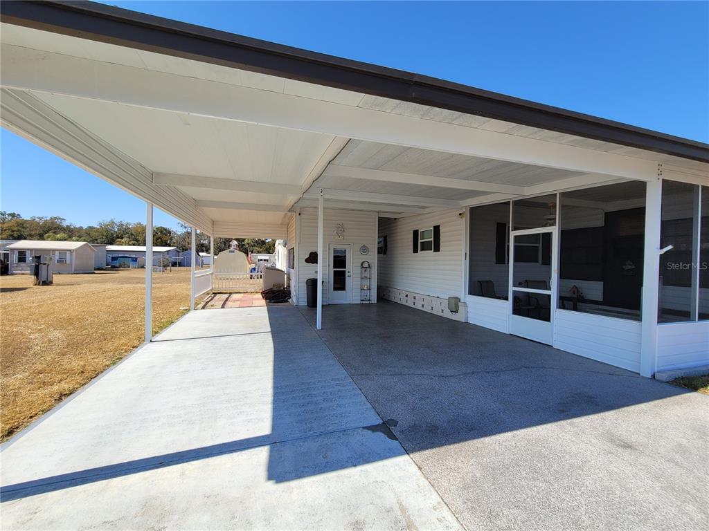 A concrete carport extends from the side of a white mobile home with a screened porch — 39438 ROCKFORD AVENUE, ZEPHYRHILLS, FL