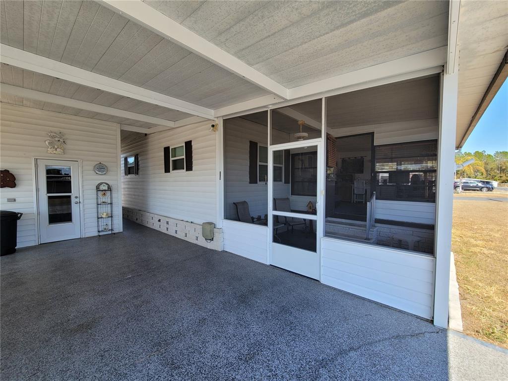 A covered concrete carport leads to a screened-in porch on a white mobile home — 39438 ROCKFORD AVENUE, ZEPHYRHILLS, FL