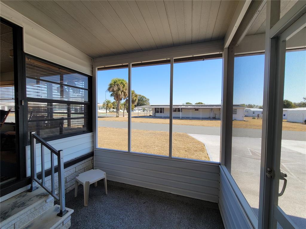 A screened-in porch with a concrete floor overlooks a street and neighboring mobile homes — 39438 ROCKFORD AVENUE, ZEPHYRHILLS, FL