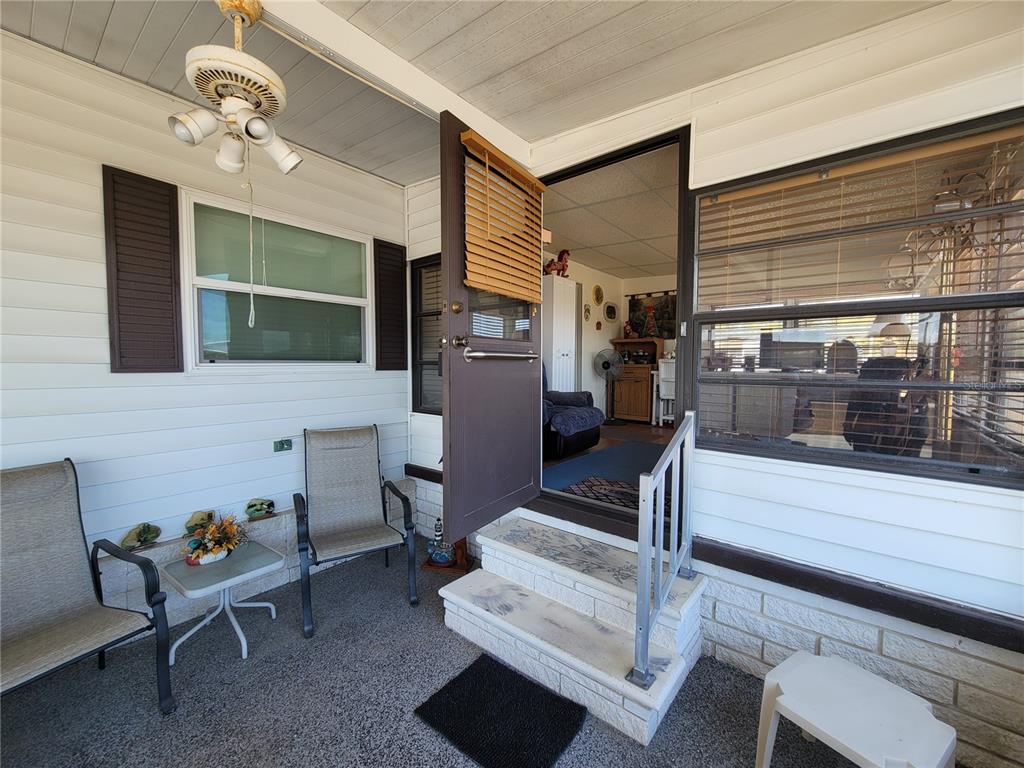 A covered porch features two chairs, a small table, and steps leading into the home — 39438 ROCKFORD AVENUE, ZEPHYRHILLS, FL