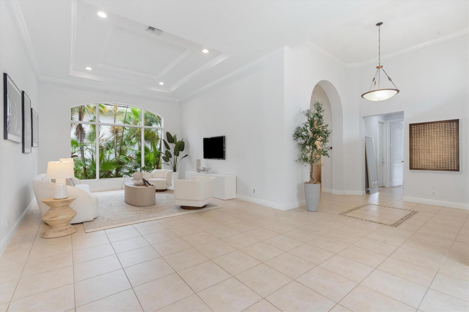 A bright, open-concept living room features white walls, tile flooring, and a large arched window — 15873 Double Eagle Trail, Delray Beach FL 33446, DELRAY BEACH, FL