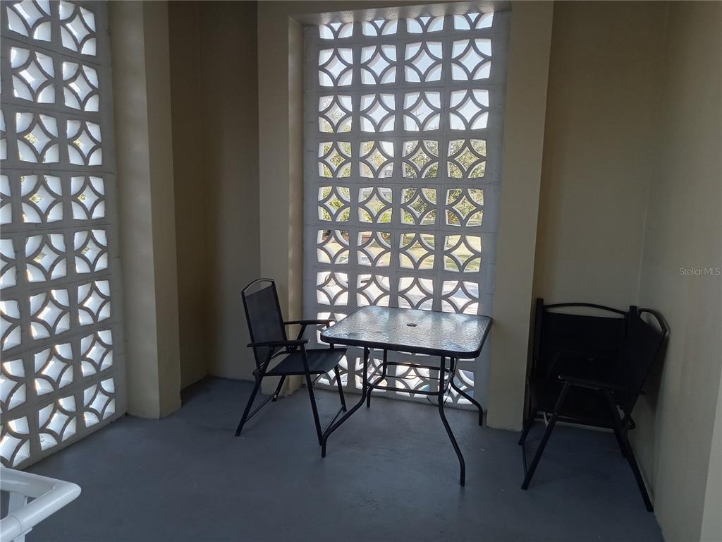 A covered patio features a glass-topped table, two chairs, and decorative concrete breeze block walls — 2331 FINLANDIA LANE UNIT 53, CLEARWATER, FL