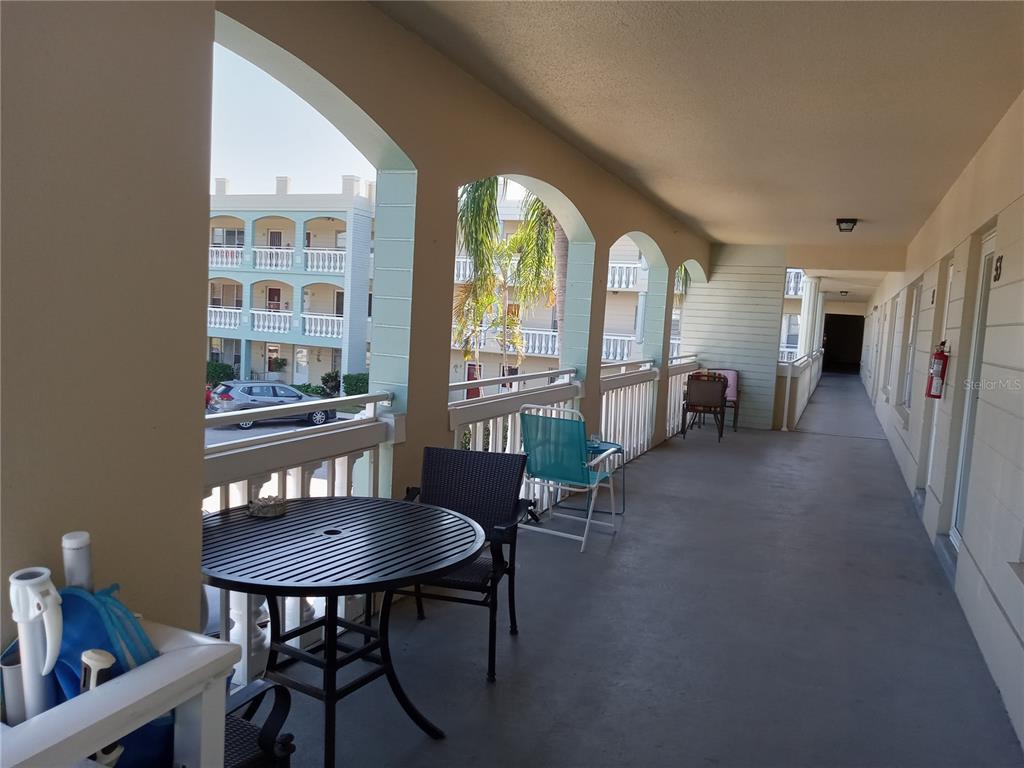 An outdoor covered walkway features a round table, chairs, and arched openings overlooking a parking lot — 2331 FINLANDIA LANE UNIT 53, CLEARWATER, FL