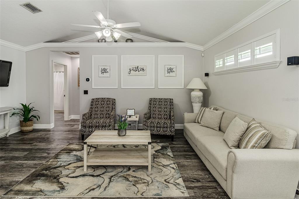 A living room features a beige sofa, two patterned armchairs, a coffee table, and wall art — 5864 MANCHESTER DRIVE W, LAKELAND, FL