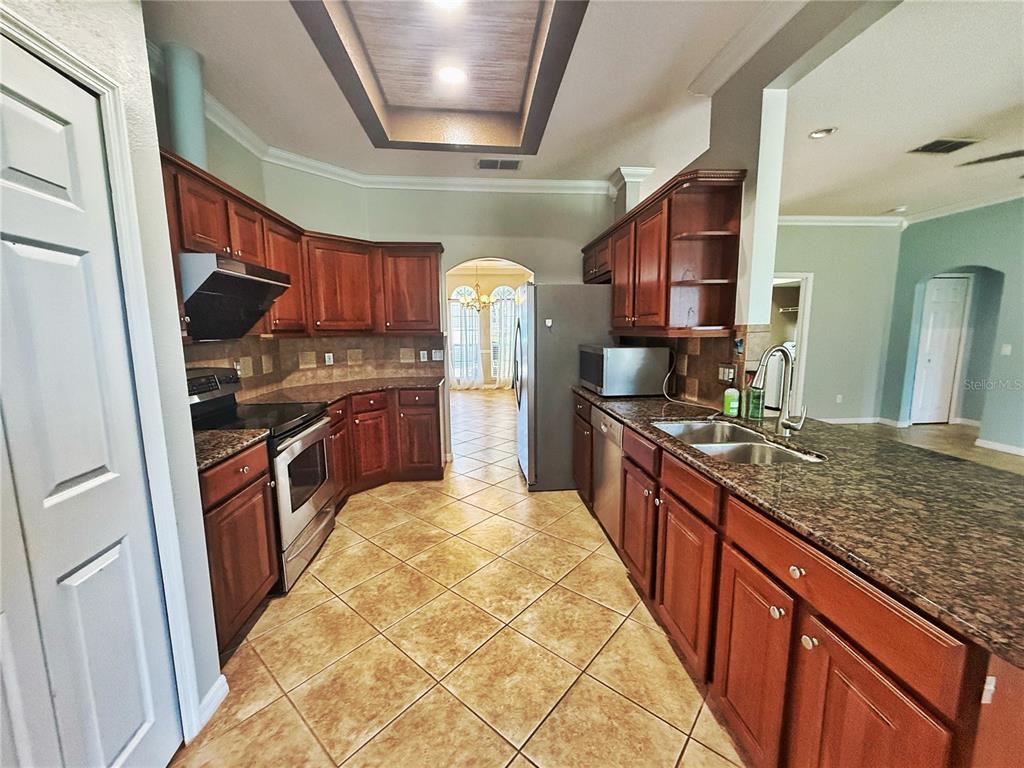 A kitchen features wood cabinets, granite countertops, stainless steel appliances, and tile flooring — 2222 CAXTON AVENUE, CLERMONT, FL