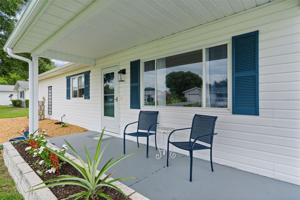 A covered front porch with two blue chairs and a small table sits before white siding — 10591 SE 178TH STREET, SUMMERFIELD, FL