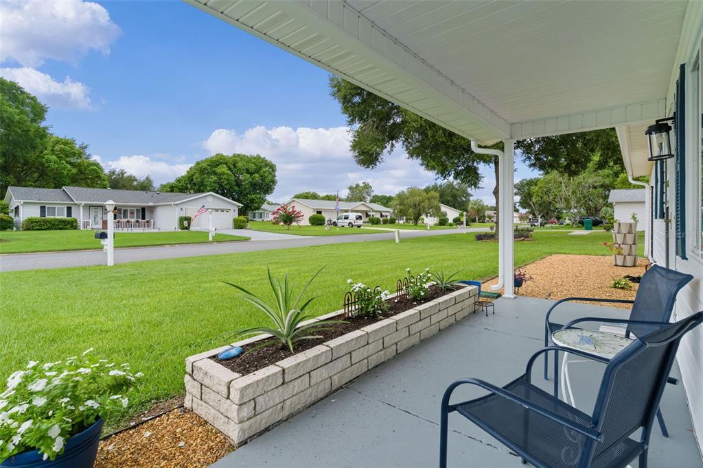 A covered front porch features a brick planter, patio chairs, and a view of neighborhood lawns — 10591 SE 178TH STREET, SUMMERFIELD, FL
