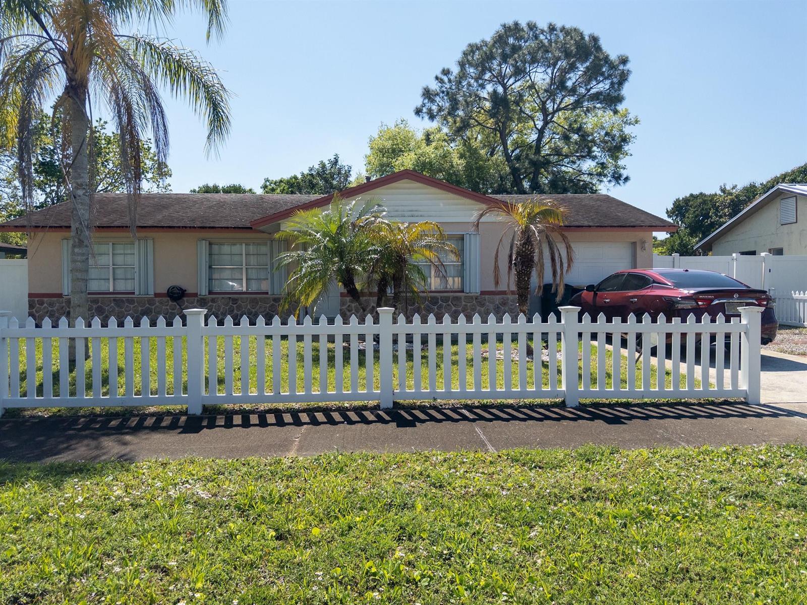 A single-story house with a white picket fence, palm trees, and a red car parked outside — 3205 Hibiscus, Fort Pierce FL 34947, FORT PIERCE, FL