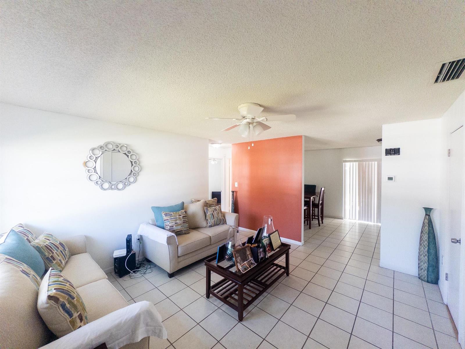 A living room with tile floors, a beige sofa, and an accent wall — 3205 Hibiscus, Fort Pierce FL 34947, FORT PIERCE, FL