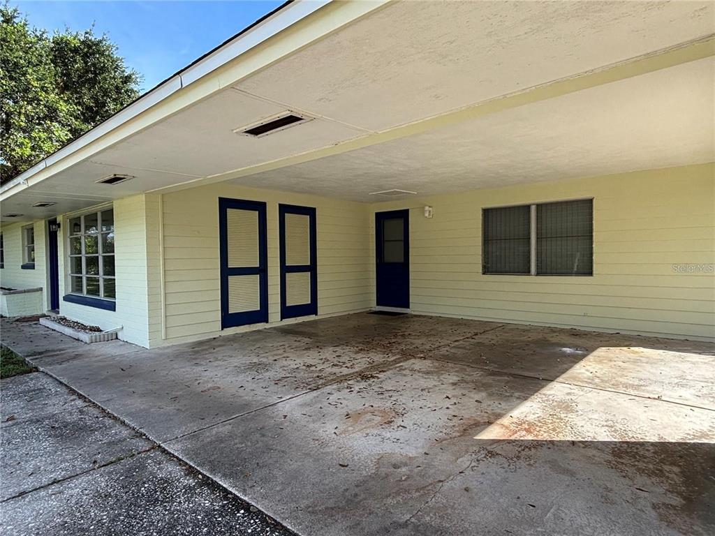 A covered concrete carport area features yellow siding, a dark blue door, and two windows — 819 E 13TH AVENUE, NEW SMYRNA BEACH, FL