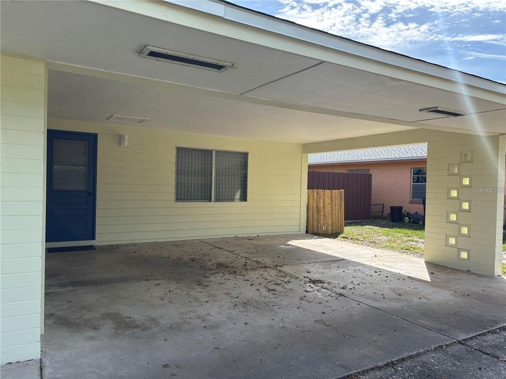 A covered carport with a concrete floor, a blue door, and decorative block wall accents — 819 E 13TH AVENUE, NEW SMYRNA BEACH, FL
