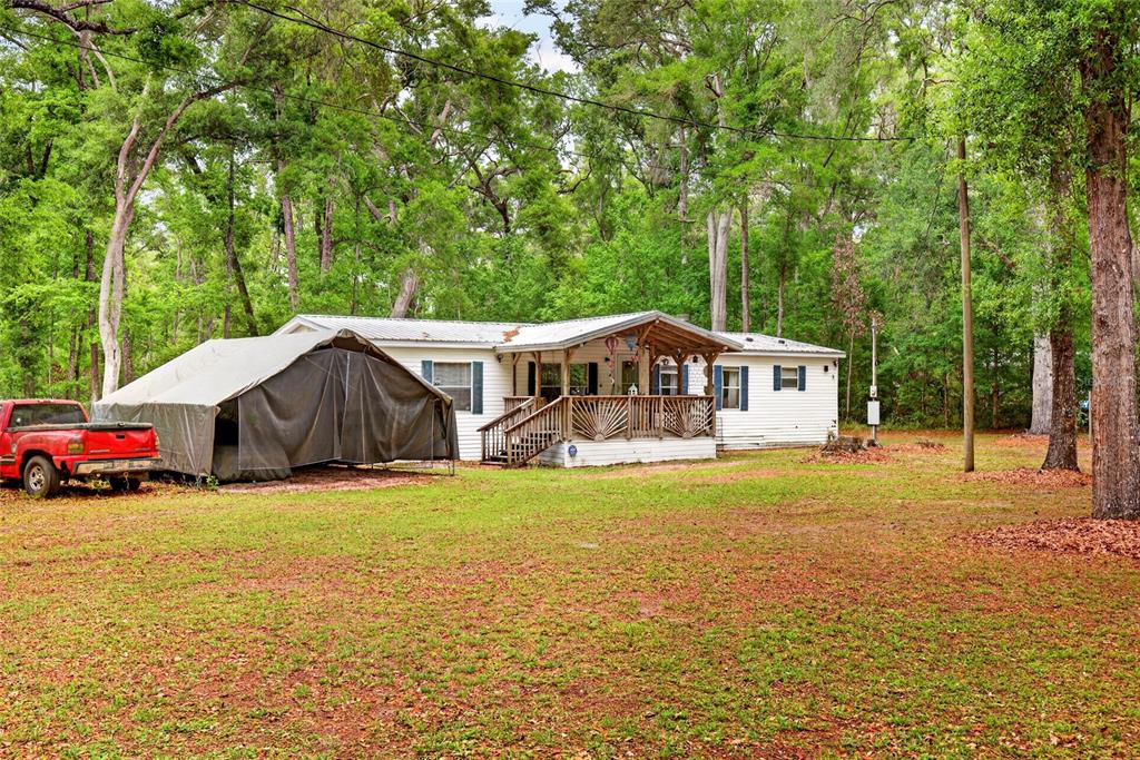 A white mobile home with a wooden porch sits in a wooded yard with a truck — 1502 NE 644TH STREET, OLD TOWN, FL