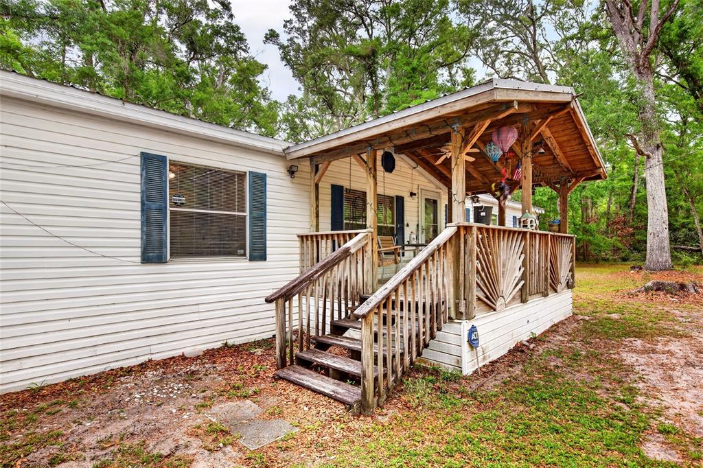 A mobile home features a wooden porch with decorative railings and stairs leading to the entrance — 1502 NE 644TH STREET, OLD TOWN, FL