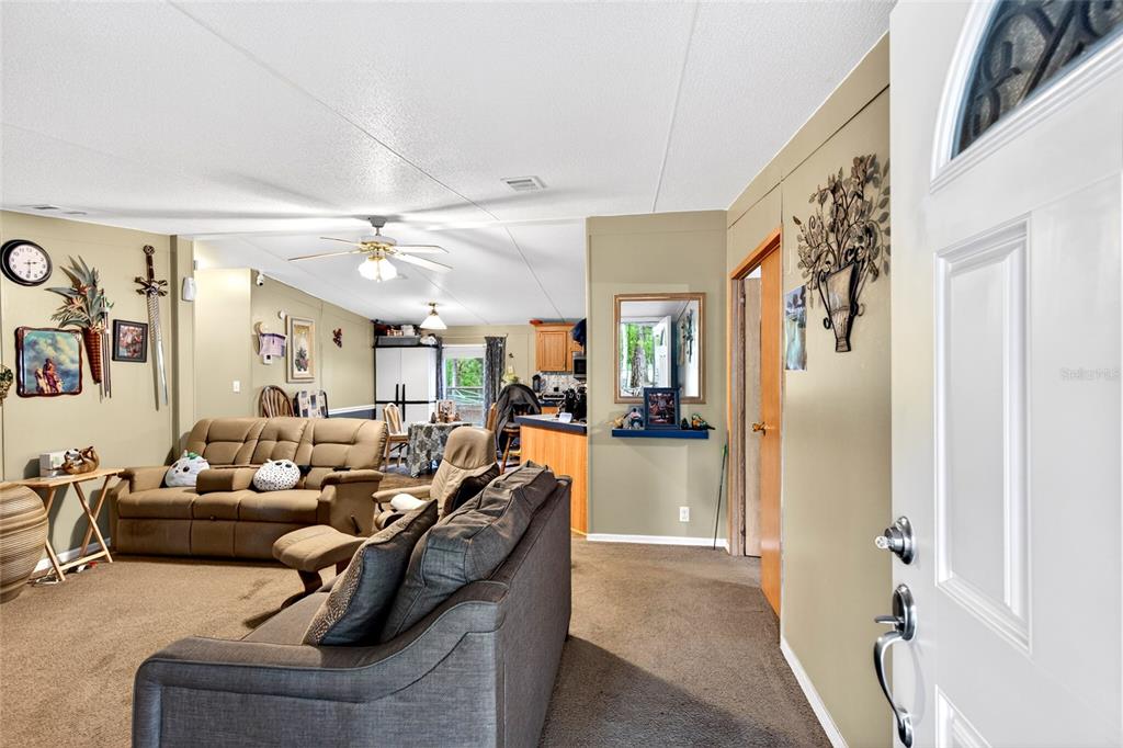A living room with carpeted floors, a tan sofa, and an open view into the kitchen — 1502 NE 644TH STREET, OLD TOWN, FL