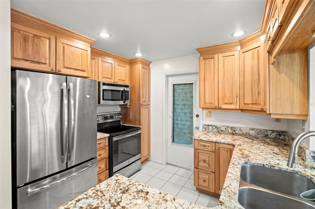 A kitchen features light wood cabinets, granite countertops, stainless steel appliances, and white tile flooring — 9306 42ND STREET N, PINELLAS PARK, FL