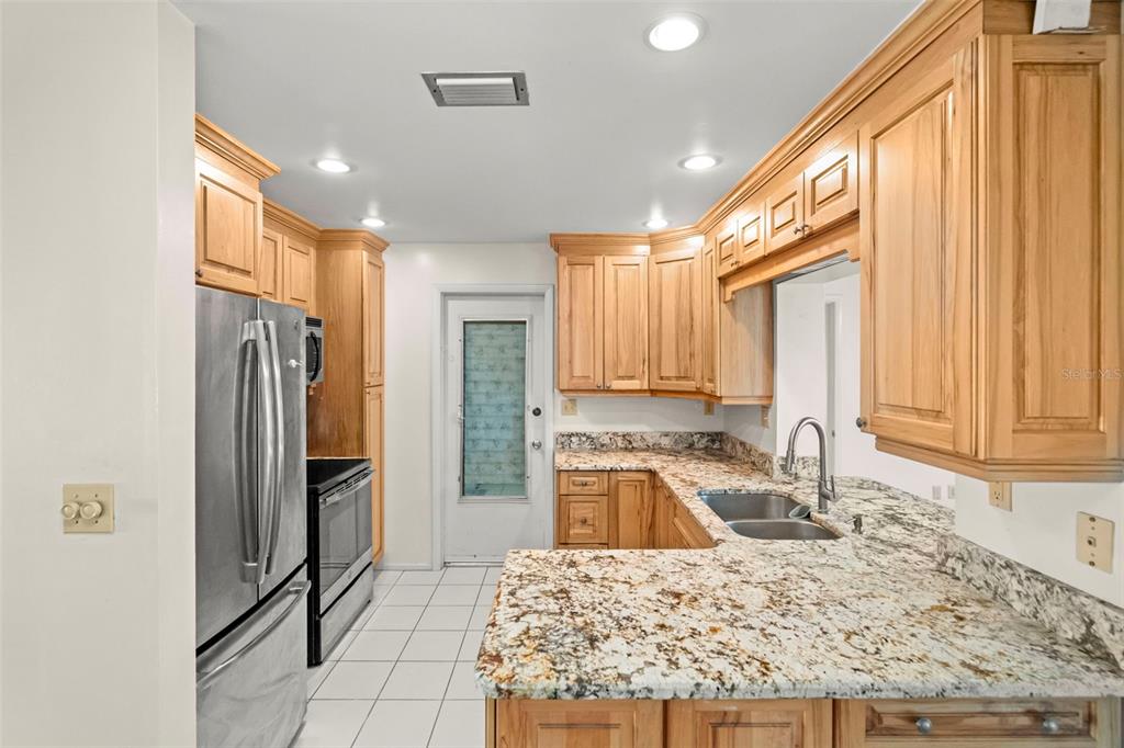 A kitchen features light wood cabinets, granite countertops, stainless steel appliances, and white tile flooring — 9306 42ND STREET N, PINELLAS PARK, FL