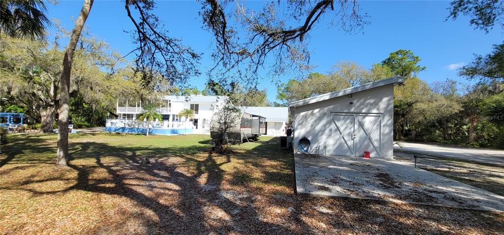 A white house and a detached garage sit on a grassy lot with trees — 6610 MCKOWN ROAD, SARASOTA, FL