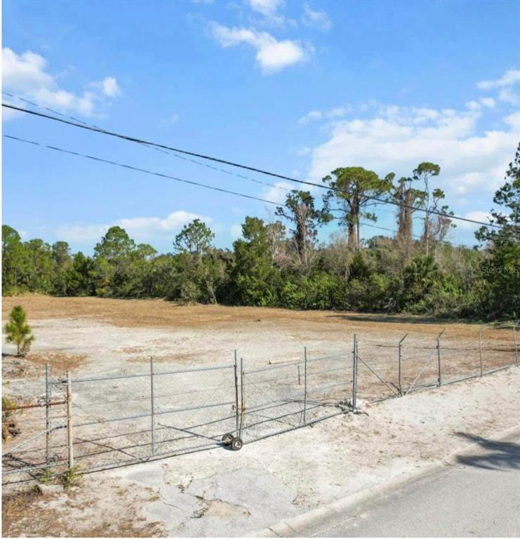 A fenced, vacant dirt lot sits beside a paved road under a blue sky — 7435 TERRACE DRIVE, HUDSON, FL