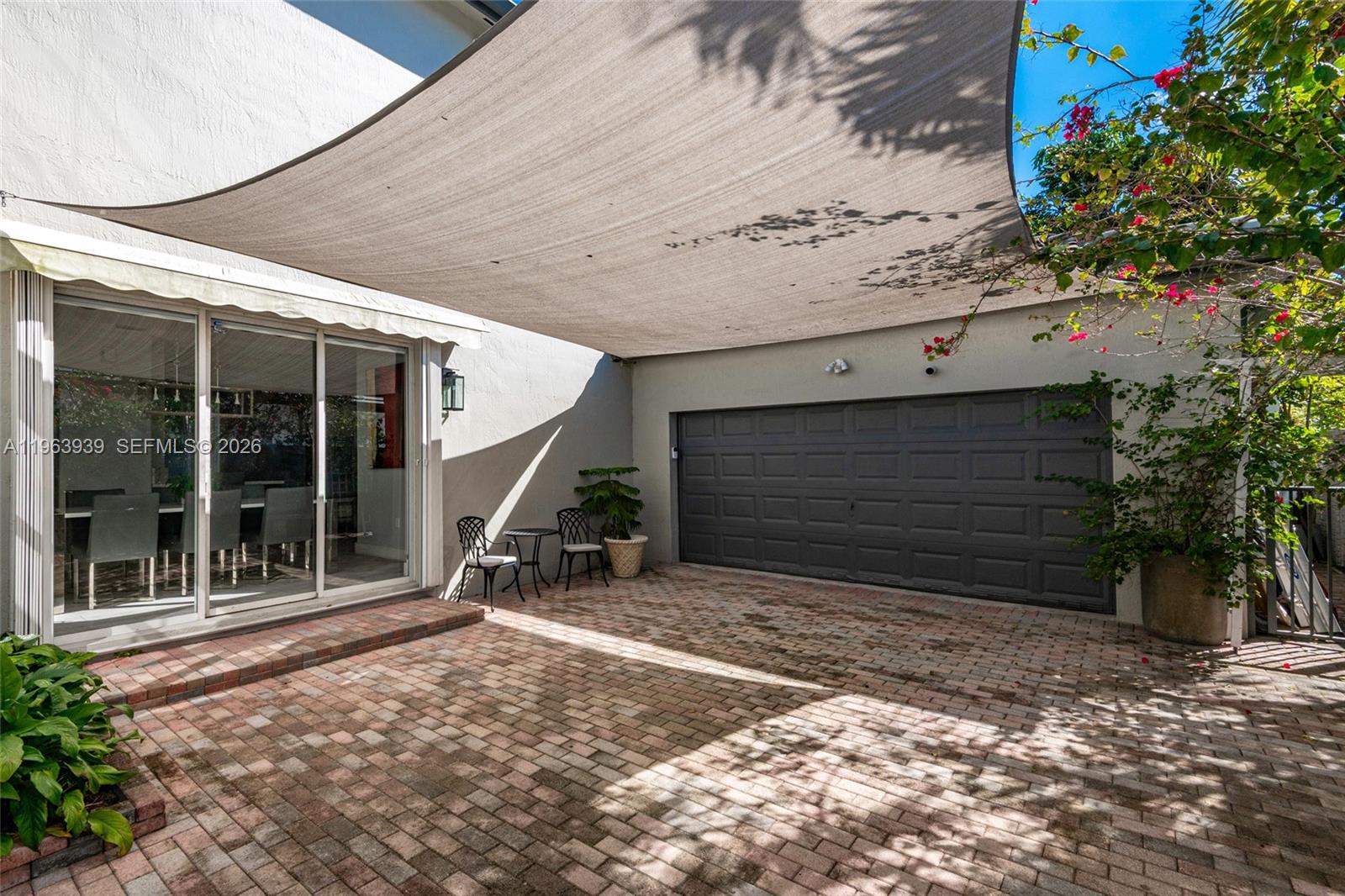 A brick-paved patio features a shade sail, a garage door, and sliding glass doors — 14900 SW 10th St, Miami FL 33194, MIAMI, FL