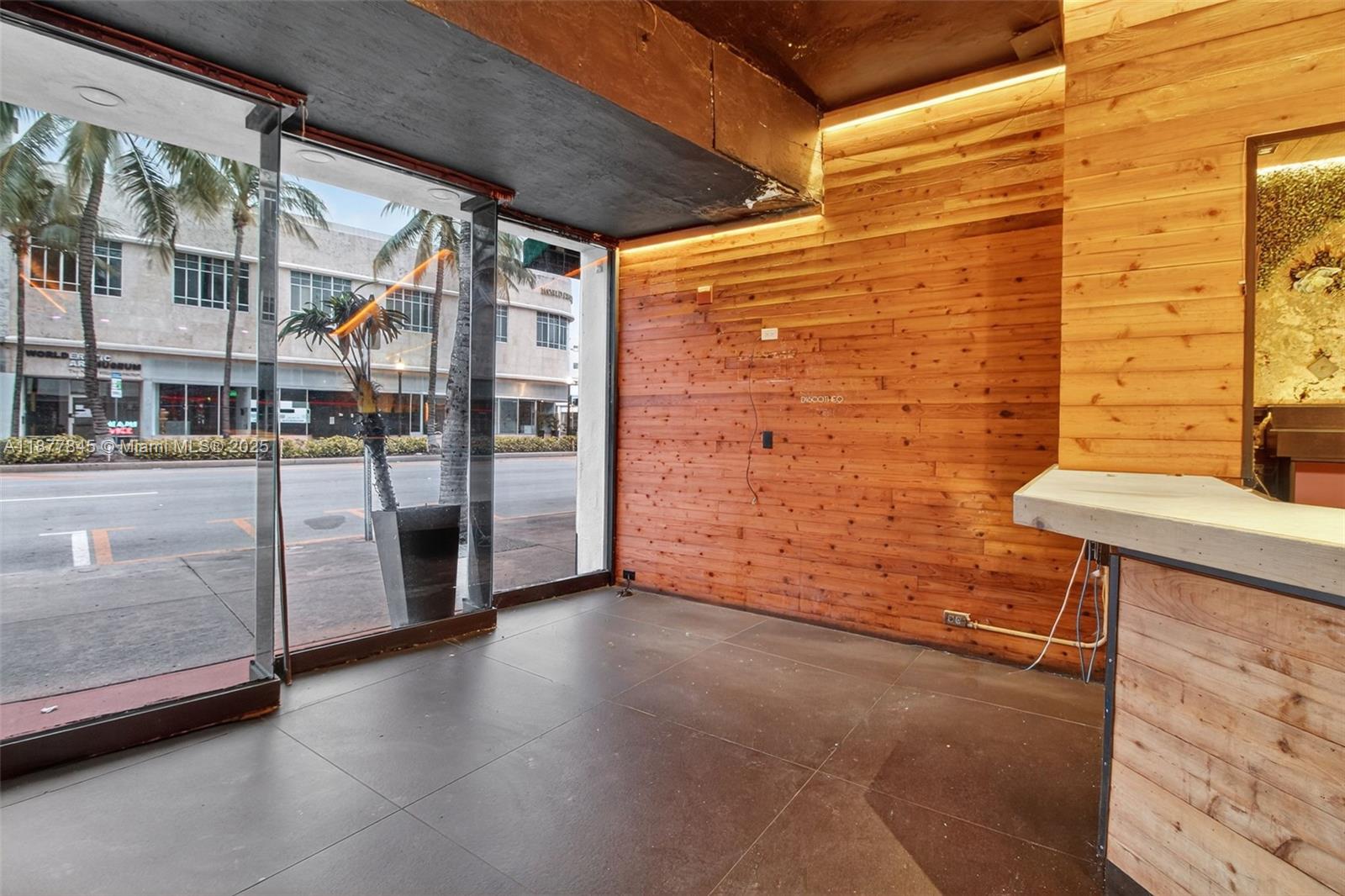 An empty commercial space features wood-paneled walls, dark tiled floors, and large street-facing windows — 1216 Washington AVE, Miami Beach FL 33139, MIAMI BEACH, FL