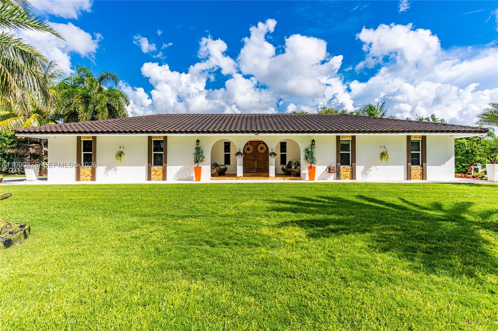 A single-story white house with a tiled roof features a central arched entryway and lawn — 18851 SW 218th St, Miami FL 33170, MIAMI, FL