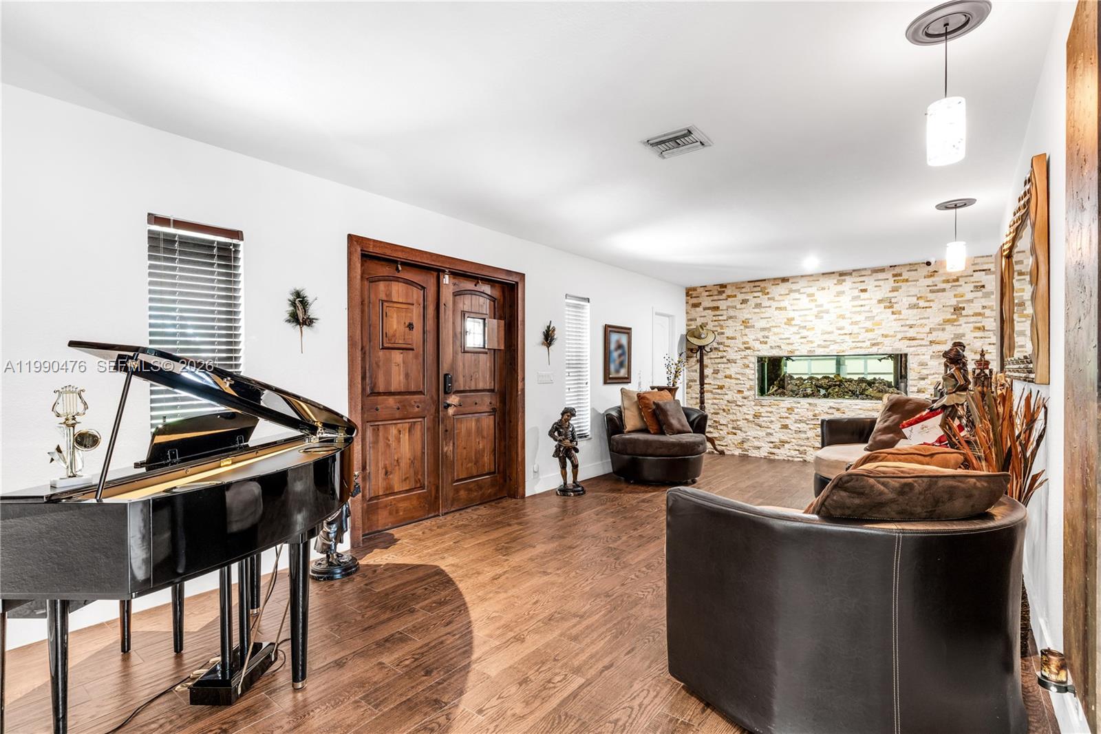 A living room features a grand piano, dark wood floors, and a stone accent wall — 18851 SW 218th St, Miami FL 33170, MIAMI, FL
