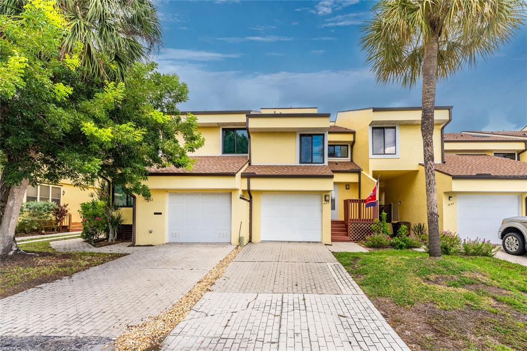 A yellow multi-unit townhouse with white garage doors and a paved driveway under palm trees — 25188 MARION AVENUE UNIT 1033, PUNTA GORDA, FL