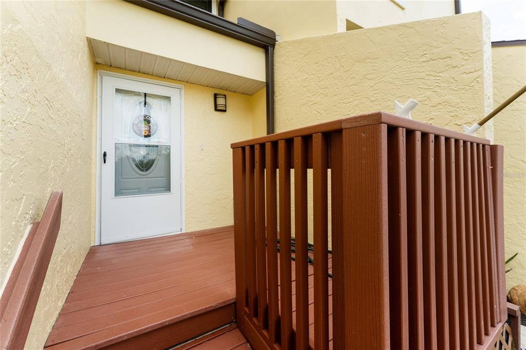 A wooden deck with a railing leads to a white front door of a house — 25188 MARION AVENUE UNIT 1033, PUNTA GORDA, FL