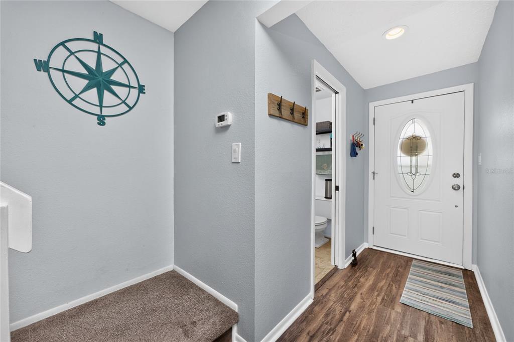 An entryway features a white front door, wood-look flooring, a compass wall decoration, and carpeted stairs — 25188 MARION AVENUE UNIT 1033, PUNTA GORDA, FL