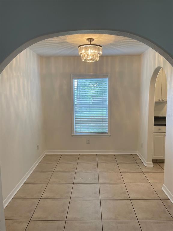 A dining area with beige tile flooring, an arched entryway, and a tiered crystal chandelier — 1914 W AILEEN STREET, TAMPA, FL