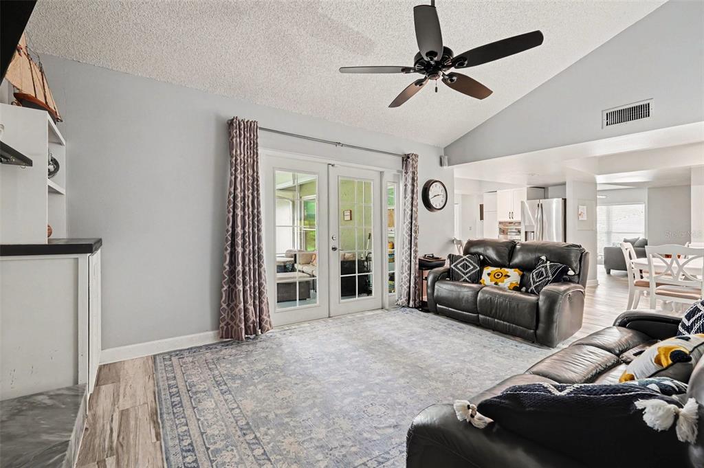 A living room with a vaulted ceiling, ceiling fan, grey rug, and dark leather sofas — 9303 ROLLING RIDGE PLACE, TAMPA, FL