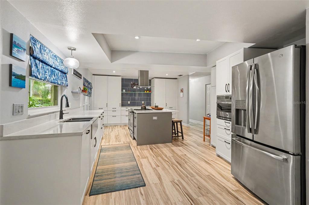 A modern kitchen features white cabinetry, a gray center island, stainless steel appliances, and wood-look flooring — 9303 ROLLING RIDGE PLACE, TAMPA, FL