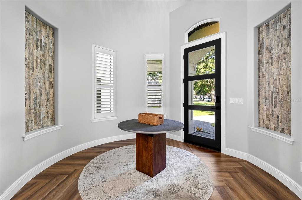 A foyer features a round table, herringbone wood floors, stone wall accents, and a glass door — 9904 BRENTFORD COURT, WINDERMERE, FL