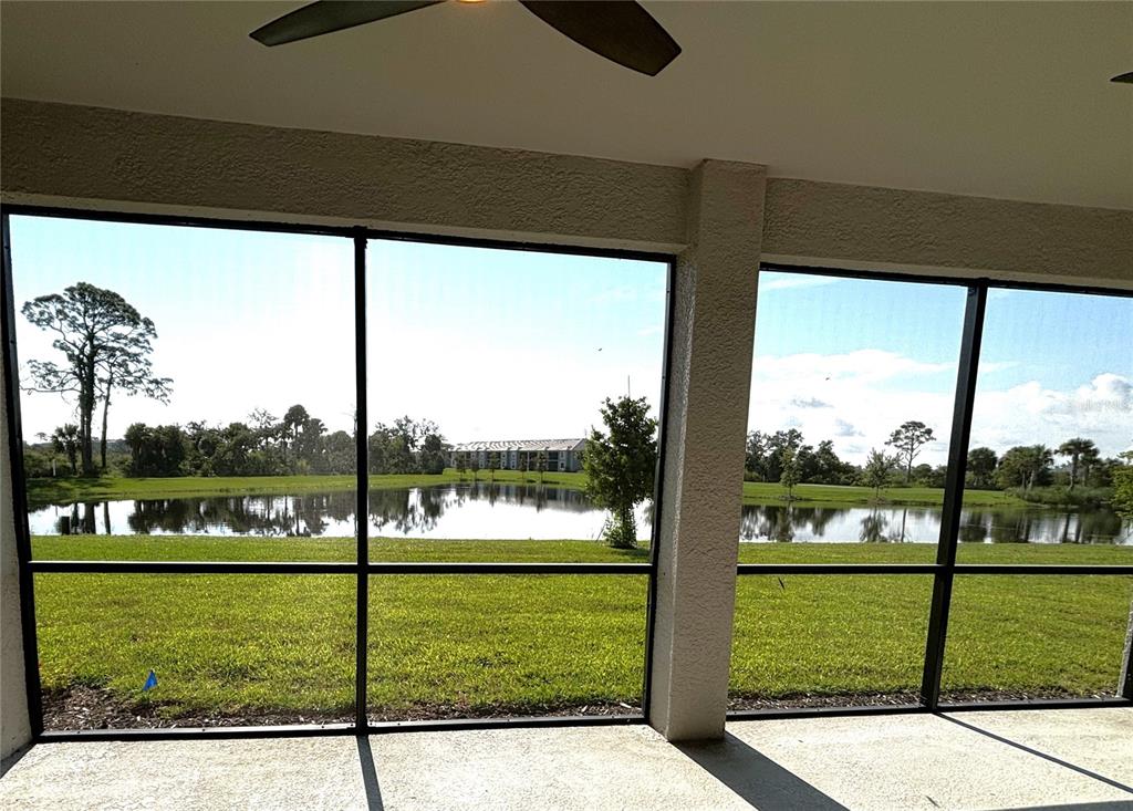 A screened-in patio overlooks a grassy lawn and a pond with distant apartment buildings — 17620 BORACAY COURT UNIT 102, VENICE, FL
