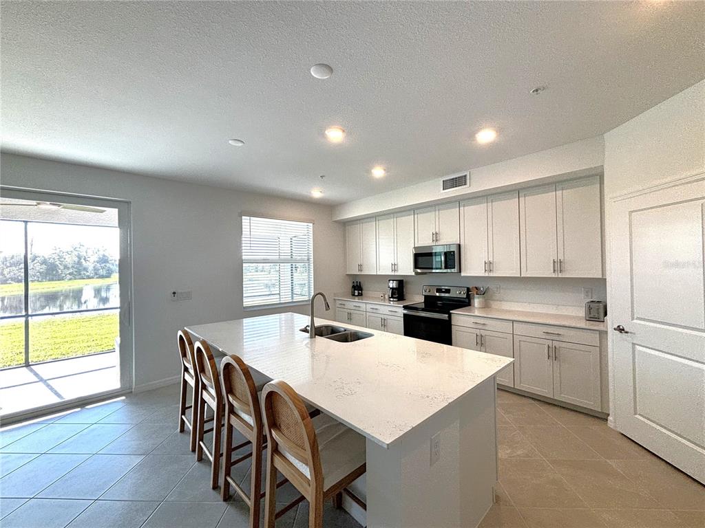 A kitchen features white cabinets, a quartz-topped island with four chairs, and a sliding door — 17620 BORACAY COURT UNIT 102, VENICE, FL