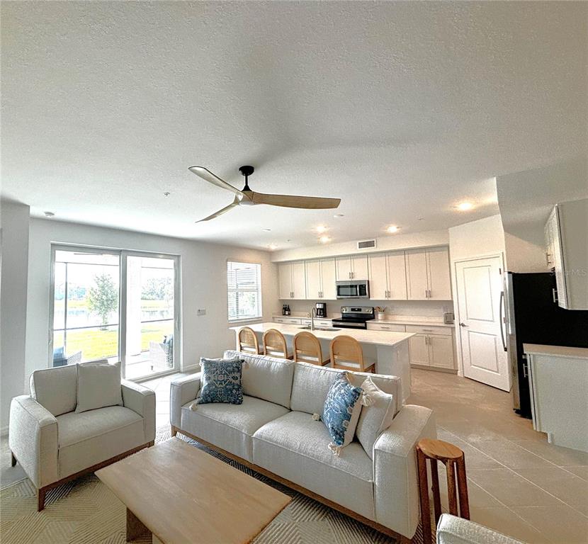 An open-concept living room and kitchen featuring light cabinetry, a central island, and sliding doors — 17620 BORACAY COURT UNIT 102, VENICE, FL
