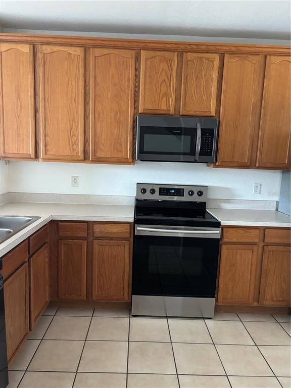 A kitchen featuring oak cabinets, stainless steel appliances, and light-colored tile flooring — 10922 SAVANNAH WOOD DRIVE UNIT 141, ORLANDO, FL