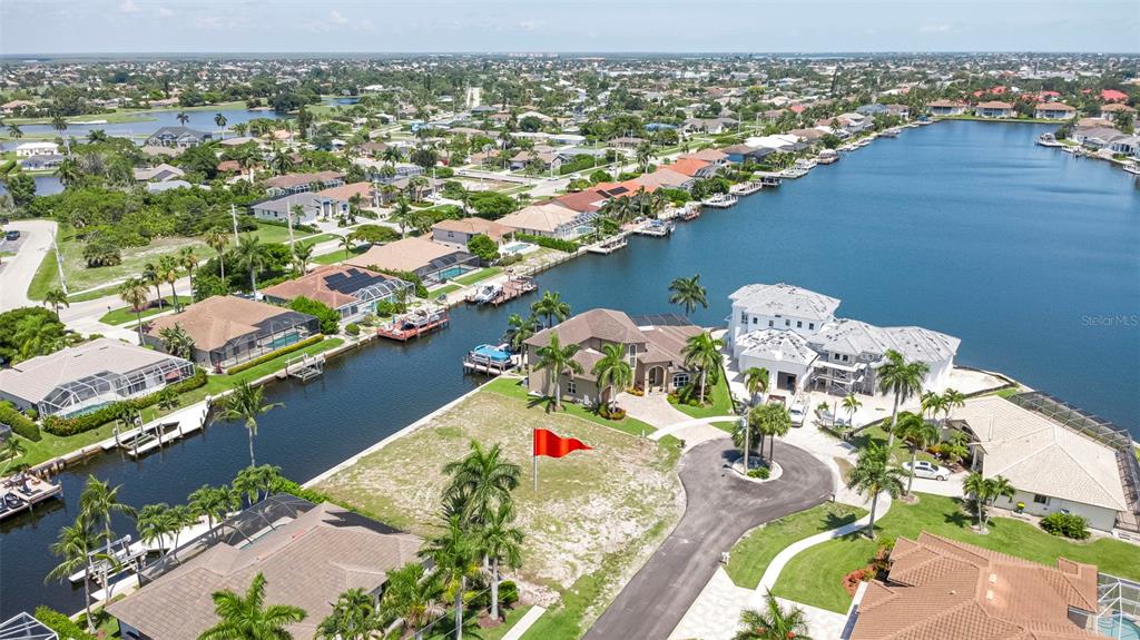 An aerial view shows a vacant waterfront lot with a red flag and nearby houses — 375 WALES COURT, MARCO ISLAND, FL