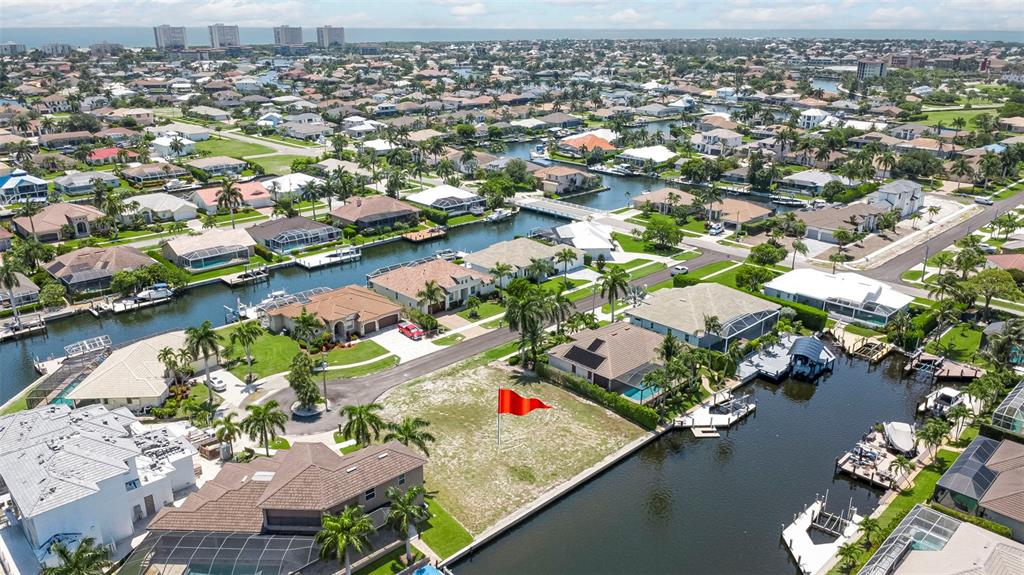 An aerial view shows a vacant waterfront lot with a red flag in a neighborhood — 375 WALES COURT, MARCO ISLAND, FL