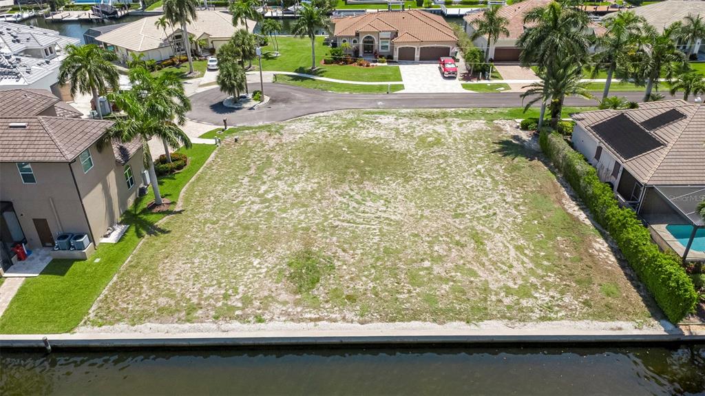 An aerial view shows a vacant waterfront lot situated between two residential homes — 375 WALES COURT, MARCO ISLAND, FL